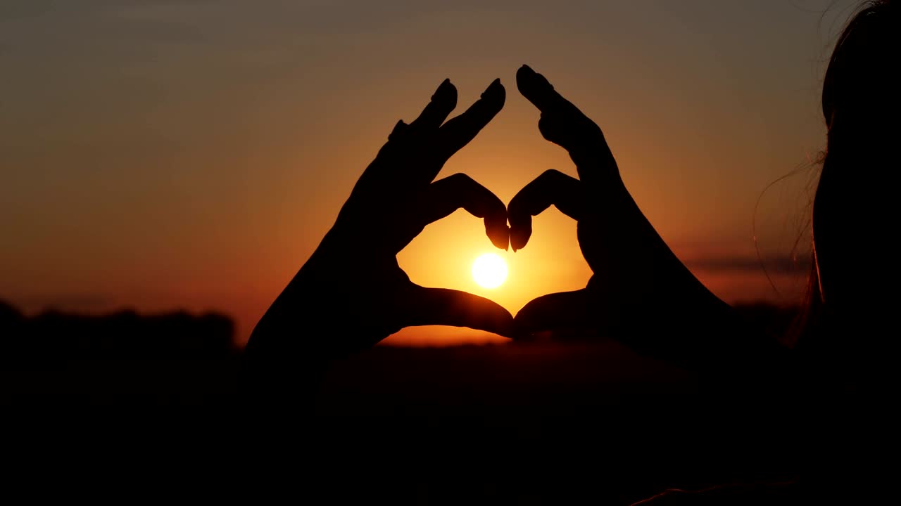 Person making heart with hands over nature sunset background