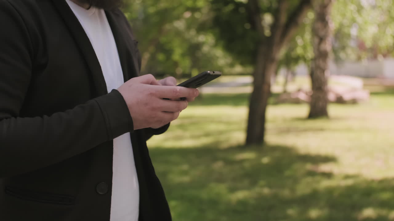 Man Walking and Typing on Mobile Phone Outdoors