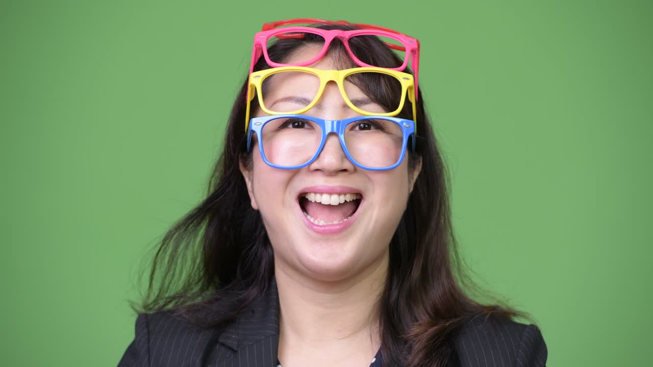 Mature beautiful Asian businesswoman wearing many eyeglasses as funny concept