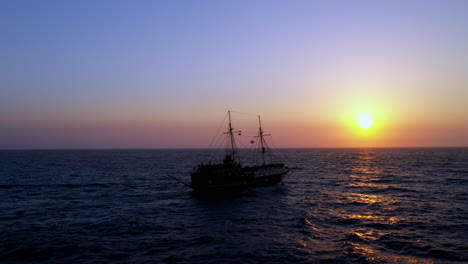 Cinematic-drone-shot-of-small-cruise-ship-sailing-into-the-sun,-following-aerial-shot