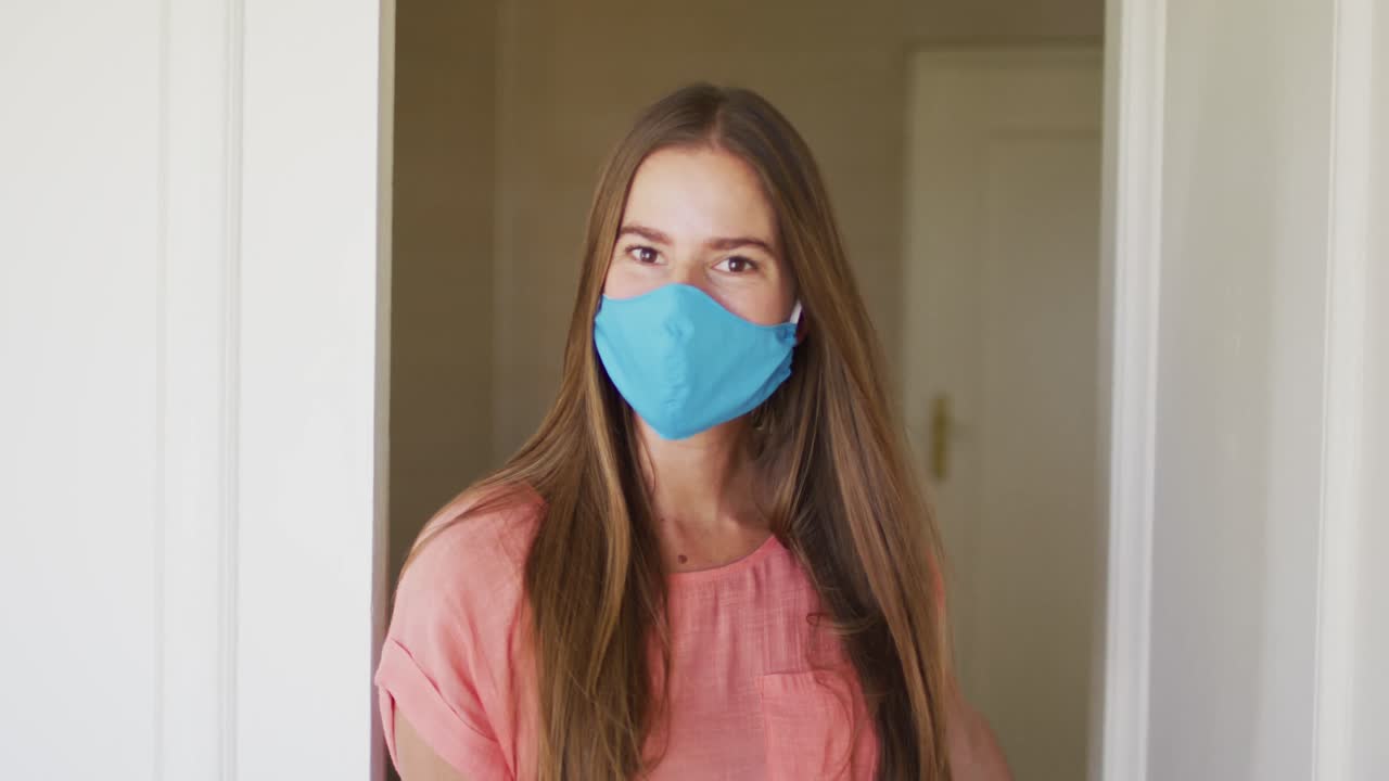 retrato de una mujer caucásica con una máscara facial abriendo el frente de la casa para dar la bienvenida a las personas