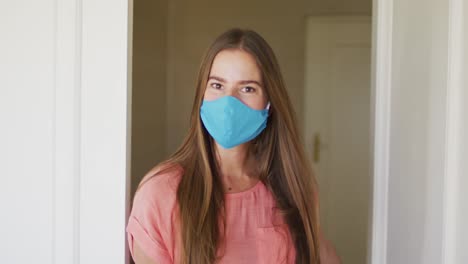 portrait of caucasian woman wearing face mask opening house front to welcome people in