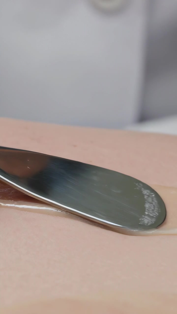 Vertical video: Placing blade above gel on skin, gloved pro in white coat dermaplaning in clinic