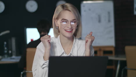 Satisfied-business-woman-rejoicing-good-results-front-laptop-in-dark-office