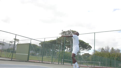 african american male tennis player serving ball on outdoor tennis court in slow motion