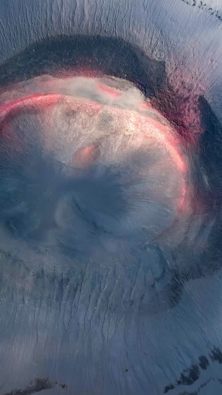 Aerial drone view of a cosmic volcanic slag cone in Iceland, showing blue crater shape and rugged lava landscape with clouds