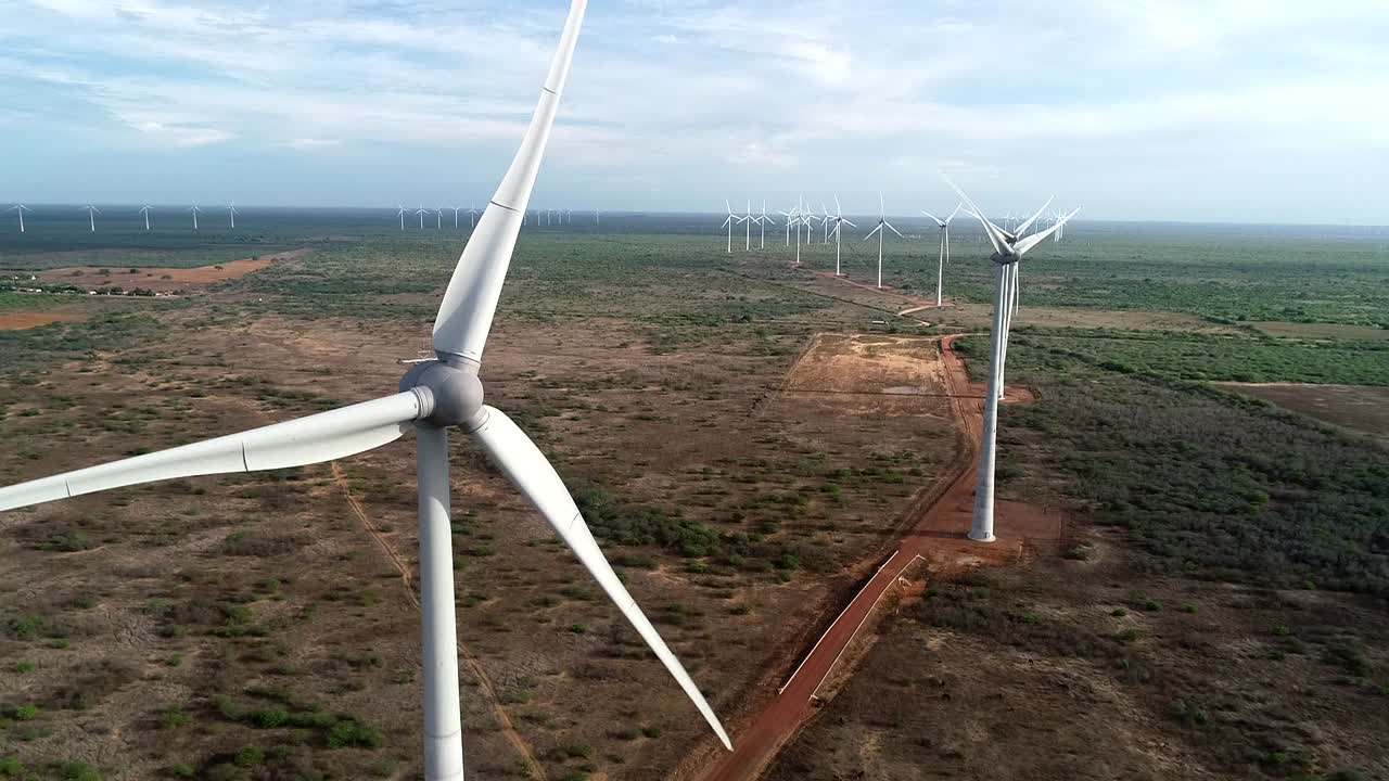 Drone filming a beautiful wind farm approaching a machine and then lateral movement towards the other wind turbines, soft light