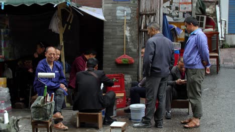five men having a work break in the middle of the day to eat, rest and talk in a back alley with a woman in the background, handheld shot