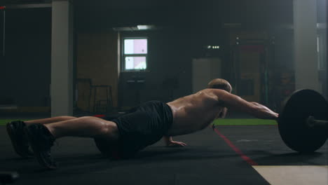 a man pushes up by rolling a barbell with one hand on the floor of the gym in slow motion