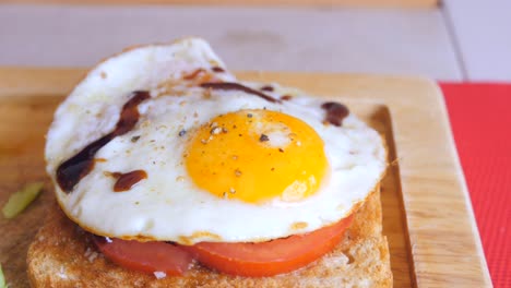 huevo estrellado sobre una tostada de pan con rodajas de tomate, condimentos y salsa balsámica