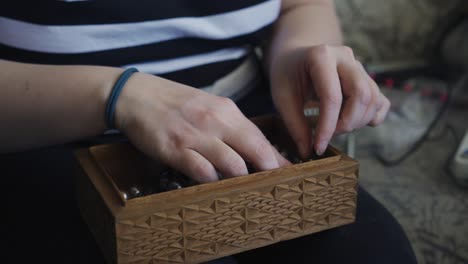 the girl takes out jewelry from a wooden box and examines them. she touches and turns them in her hands.