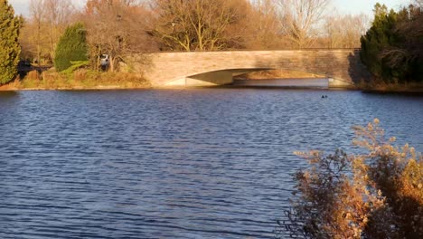 Strong-wind-currents-create-ripples-on-a-river,-with-a-brick-and-concrete-bridge-in-the-background