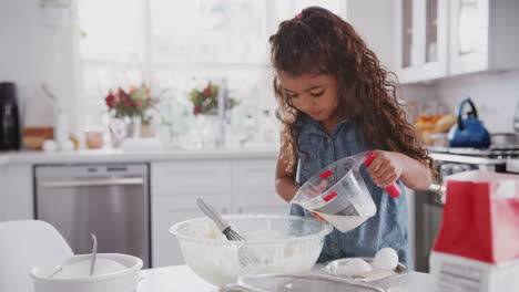 Young-girl-in-the-kitchen-preparing-cake-mixture-on-her-own,-adding-milk-and-mixing,-front-view