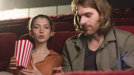 happy couple sitting in the cinema while they talking and eating popcorn waiting fot watch the film