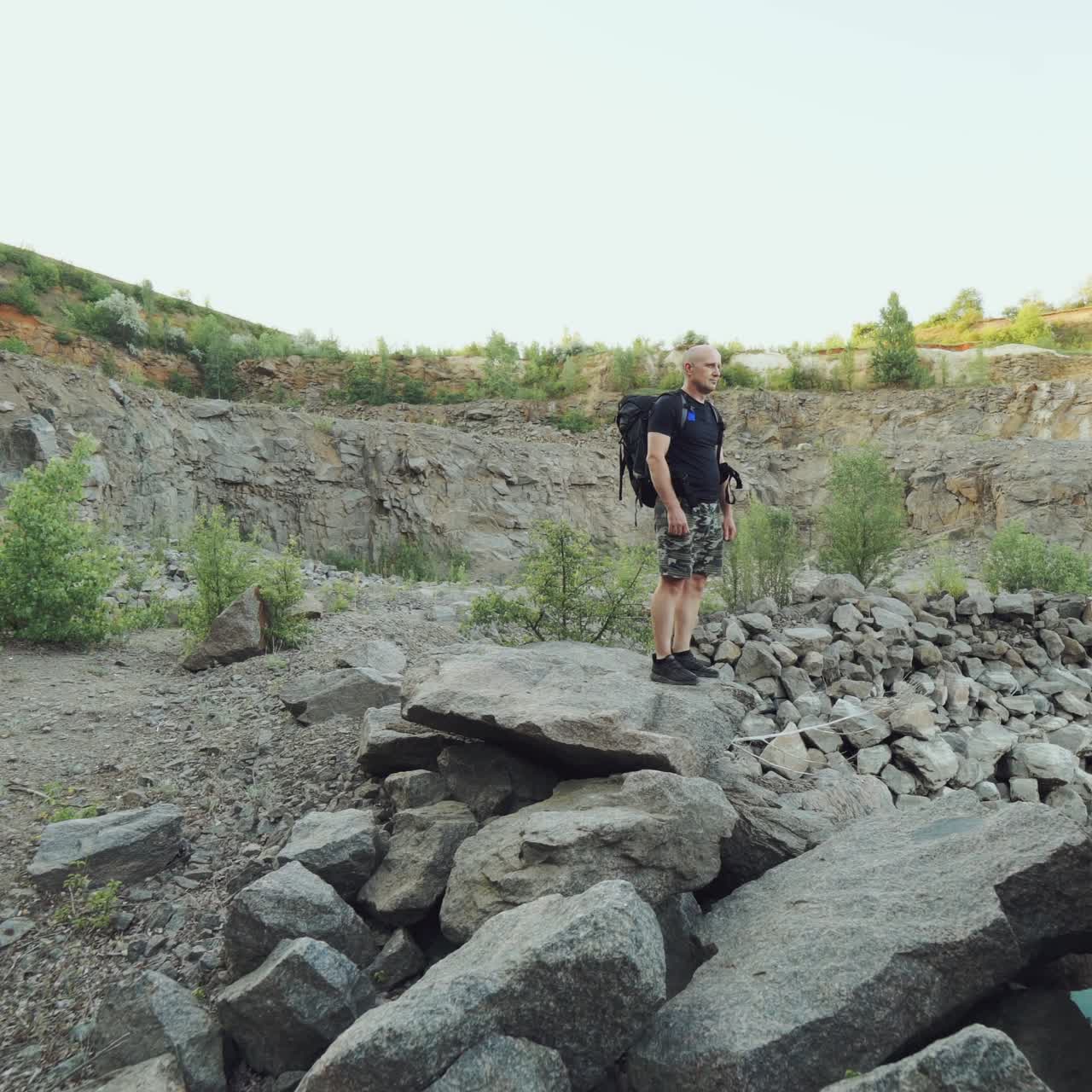 adult traveler with backpack is examining the terrain by the river and walking along the rocks along the bank on the background of a wonderful landscape