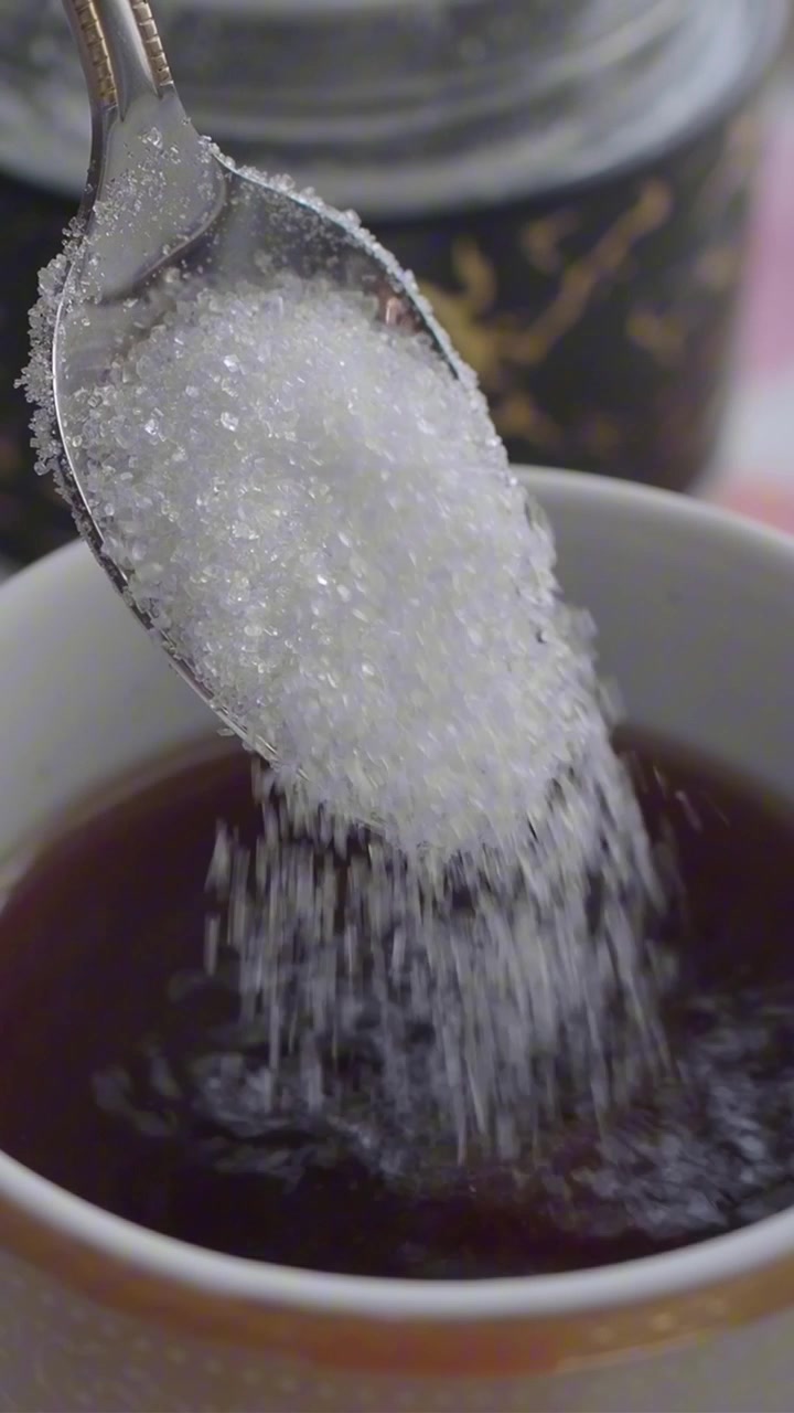 Açúcar branco caindo de uma colher em uma xícara de chá preto.