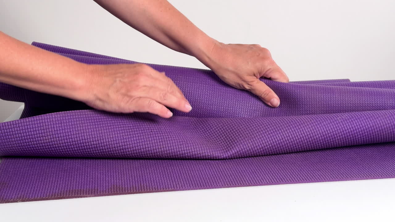 Hands Rolling Up a Purple Yoga Mat