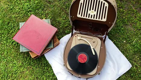 la vista superior de un viejo reproductor de discos retro de los años 50 y 60 se usa afuera en el jardín para reproducir música de un viejo disco de vinilo y al lado hay una pila de viejos discos de vinilo