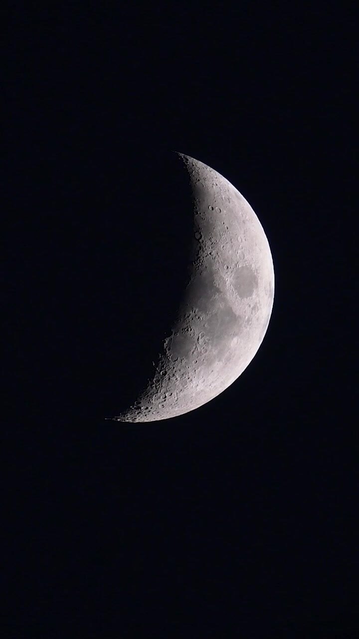 Fase detalhada da lua crescente brilhando intensamente no céu noturno escuro, vista aproximada com teleobjetiva de crateras lunares e superfície contra o espaço totalmente escuro