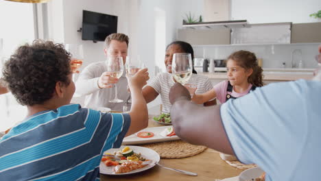 multi-generation mixed race family making a toast before eating meal around table at home together