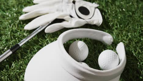 close up of golf club, balls, glove and peaked cap on grass, slow motion