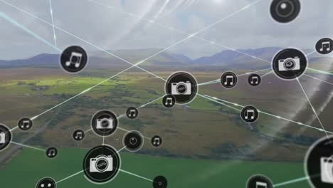 animation of icons connected with lines, aerial view of green field against mountains and cloudy sky