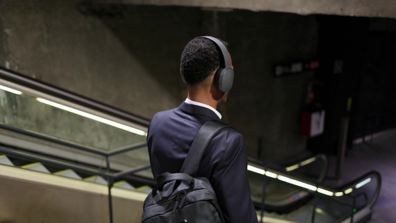 Young Man With Headphones Walking Down Stairs in Modern Subway Station