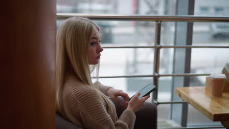 lady in woven sweater sitting contemplative on modern chair in mall, coffee on table, iron rail in background, urban mall setting with soft lighting creating peaceful reflective mood