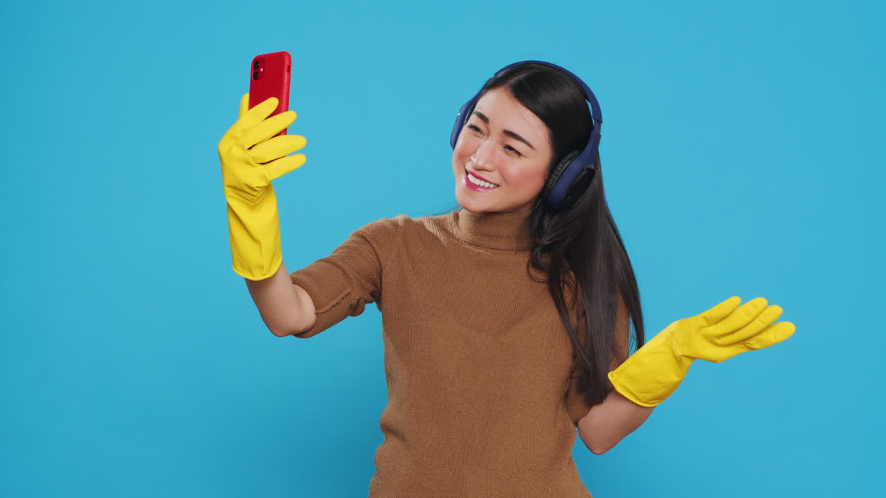Smiling asian maid wearing headphone while talking with remote friend during videocall meeting on phone