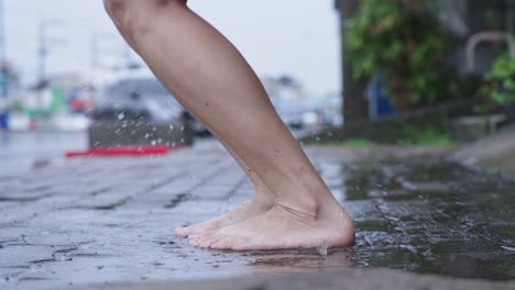 close up light skin asian girl barefoot stomp and playing on  puddles on the raining day, wet and humid tropical weather in asia, street side area, fun time splashing water, jumping goofy around