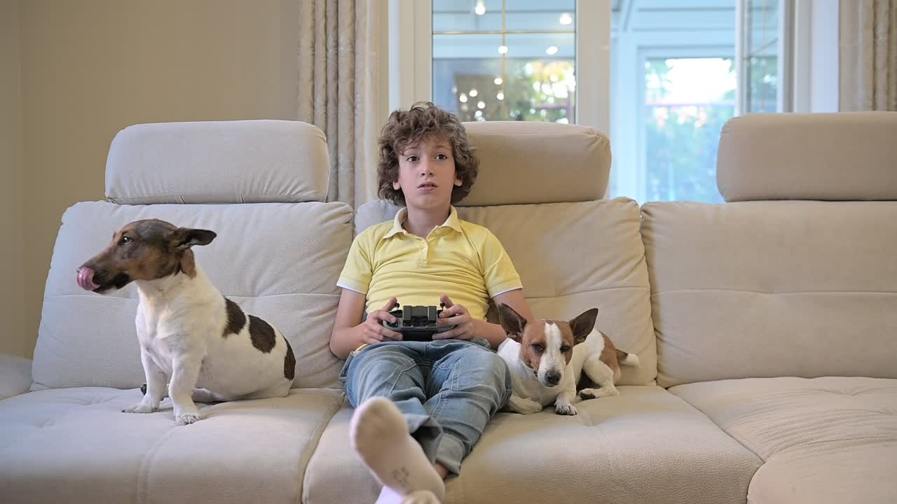 리모콘을 가지고 노는 곱슬머리의 금발 소년, 그 옆에는 그들의 개가 누워 있다