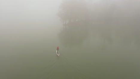 alone man is floating on a board on a river in a very thick fog