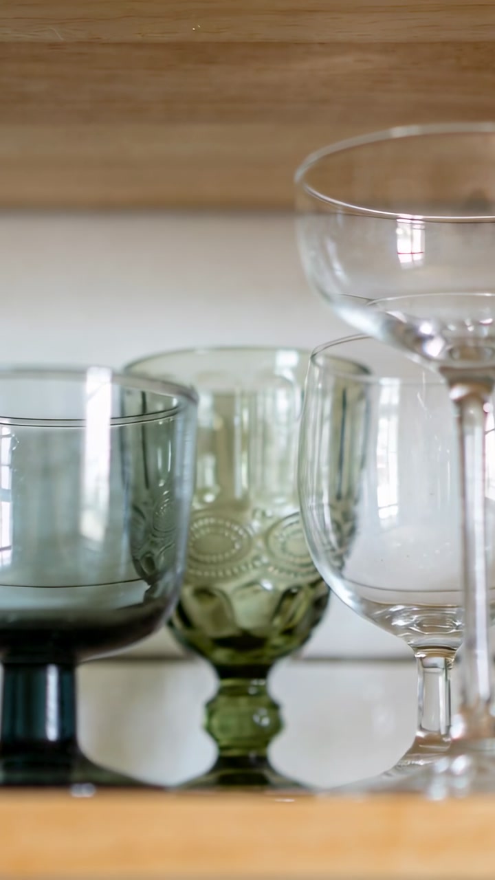 Vertical video: Sliding camera centering green goblet on shelf at home, smoky bowl and clear coupe