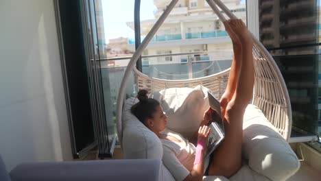 woman working on laptop in hanging chair on balcony