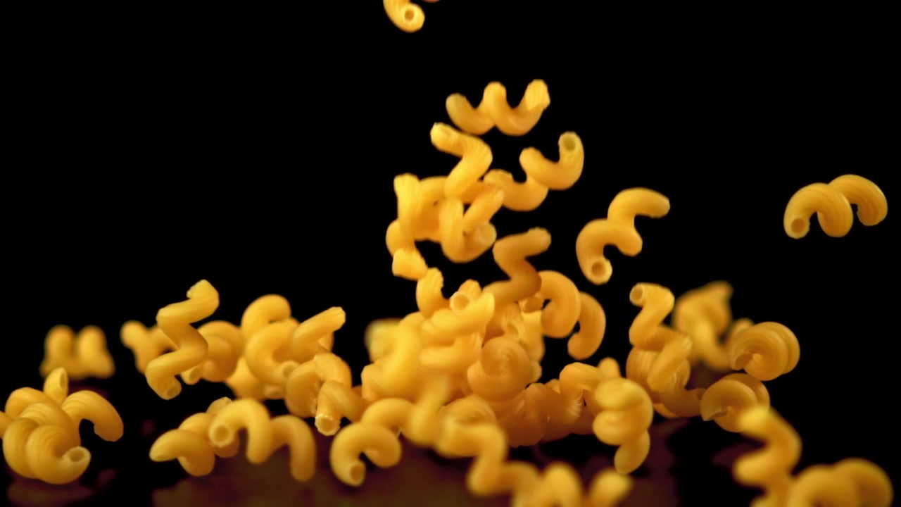 Pasta a spirale cruda che cade al rallentatore su sfondo nero