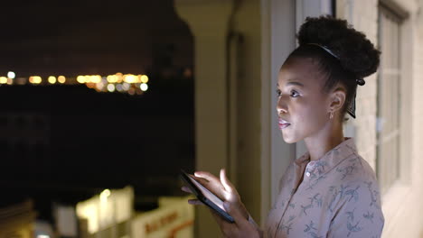 Afroamerikanische-Frau-Nutzt-Nachts-Auf-Einem-Balkon-Ein-Tablet-Mit-Kopierplatz