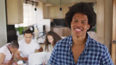 Glücklicher-Afroamerikanischer-Mann-In-Der-Küche-Mit-Verschiedenen-Freunden,-Die-Im-Hintergrund-Arbeiten