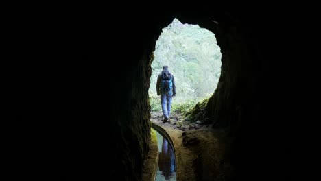 man walking out of small tunnel under mountain in madeira island