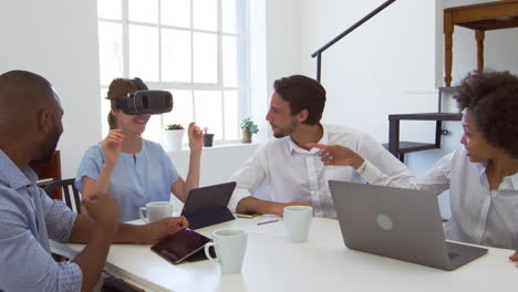 Frau-Mit-VR-Brille-An-Einem-Schreibtisch-Mit-Kollegen-In-Einem-Büro