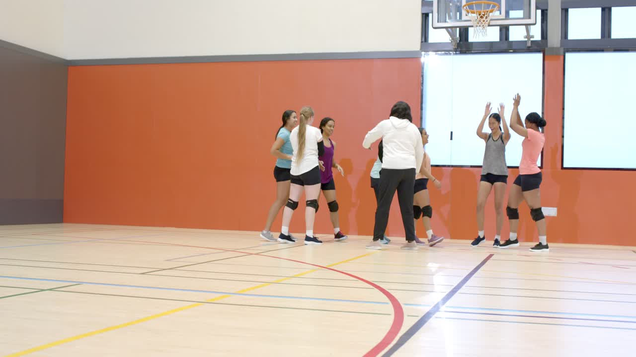 Squadra di pallavolo femminile mista che segue l'allenatore alzando le braccia, scambiandosi il cinque e unendosi in cerchio in palestra.