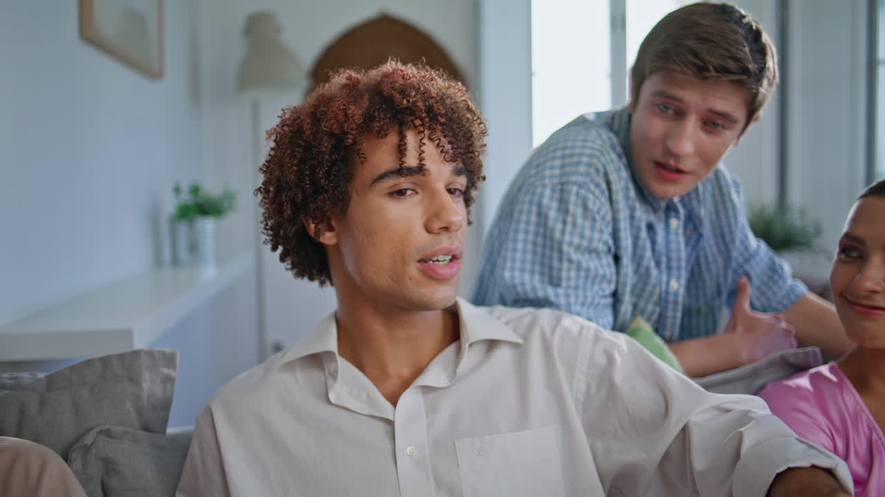 Closeup curly youngster communicating friends at living room. Buddies sitting