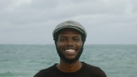 El-Primer-Plano-De-Un-Joven-Africano-Negro-Con-Barba-Guapo-Sonriendo-Con-El-Océano-De-Fondo