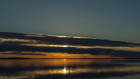 Beautiful-sunset-time-lapse-view-of-flat-surface-of-large-lake-in-Northern-Ontario-with-fishermen-in-boat-motoring-through-the-scene-before-sun-drops-below-the-horizon