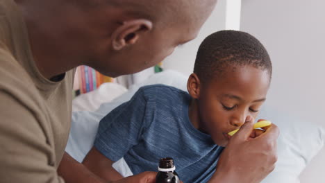 Father-Giving-Sick-Son-Ill-In-Bed-At-Home-Medicine-From-Bottle