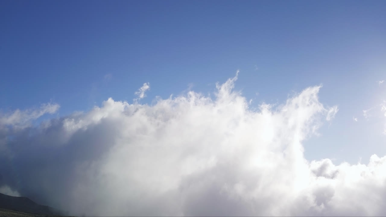 Aerial view of clouds moving over the side of a mountain on a sunny day. Maui, Hawaii.