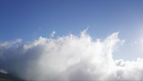 aerial view of clouds moving over the side of a mountain on a sunny day. maui, hawaii.