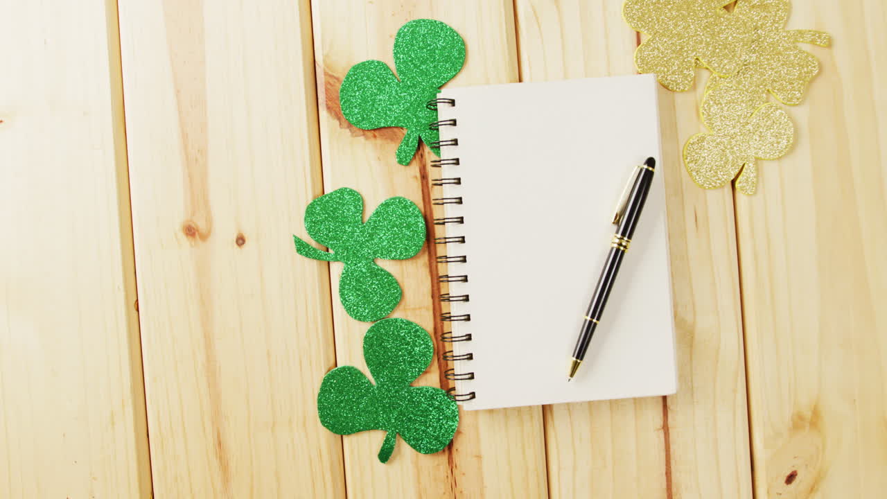 Video of st patrick's green shamrock and notebook with copy space on wooden background