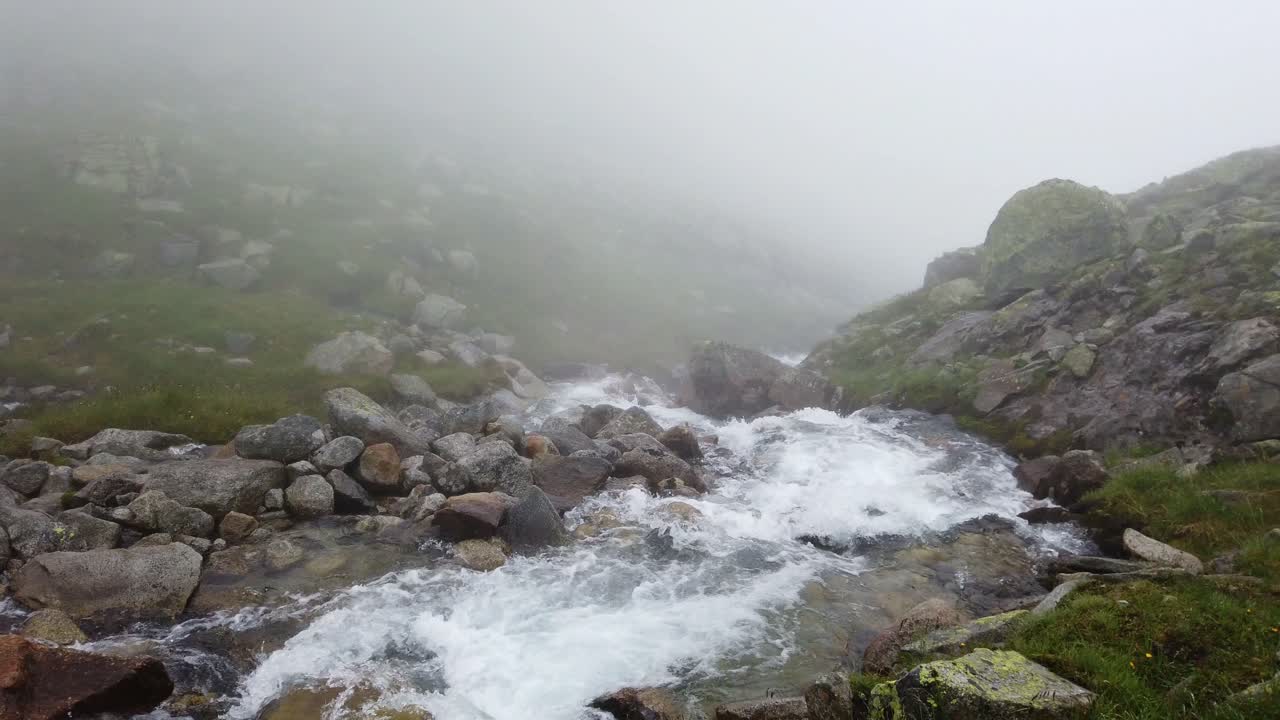 Vista estática de un arroyo alpino de rápido caudal un día lluvioso y con niebla en terreno montañoso accidentado