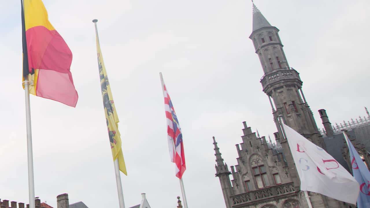 Colorful flags flutter above historic gabled rooftops and stone towers under bright daylight skies