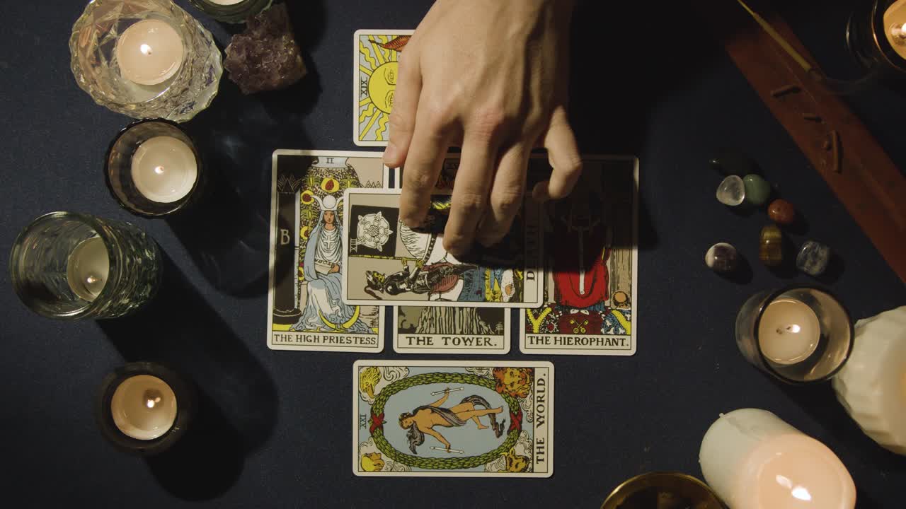 toma aérea de una persona que hace una lectura de cartas del tarot colocando cartas en la mesa con velas y cristales 3